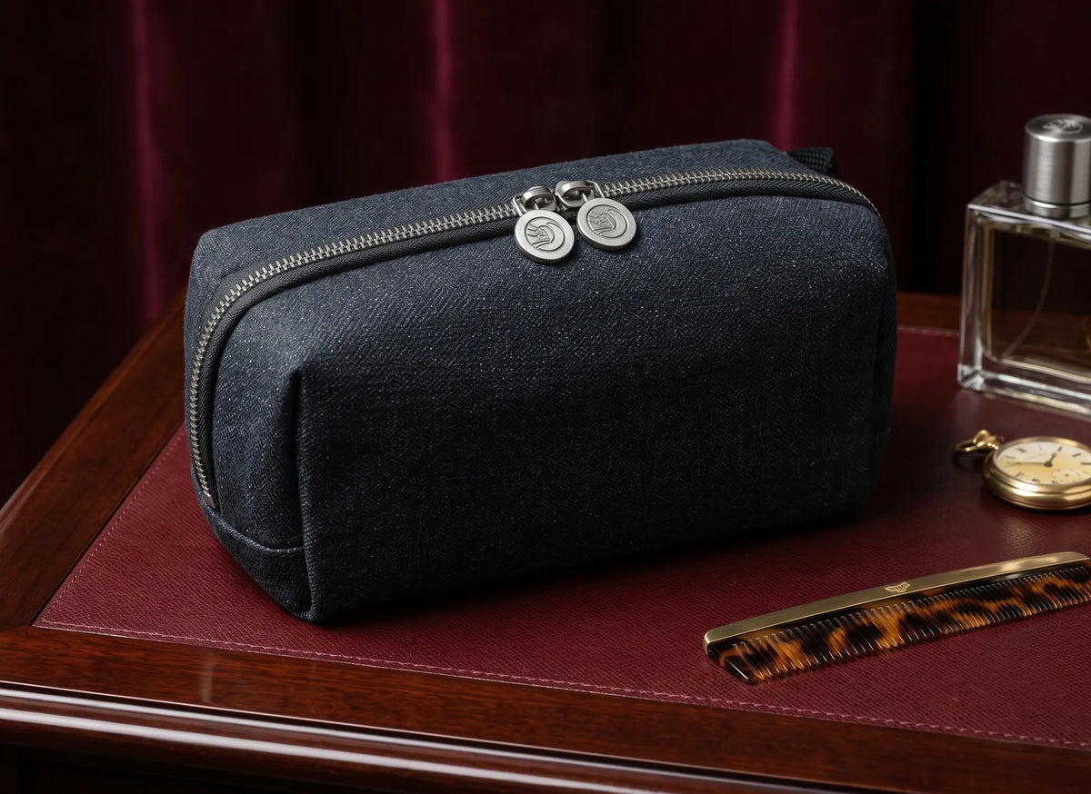 Navy denim toiletry pouch with metal zip pulls on a leather-topped desk.